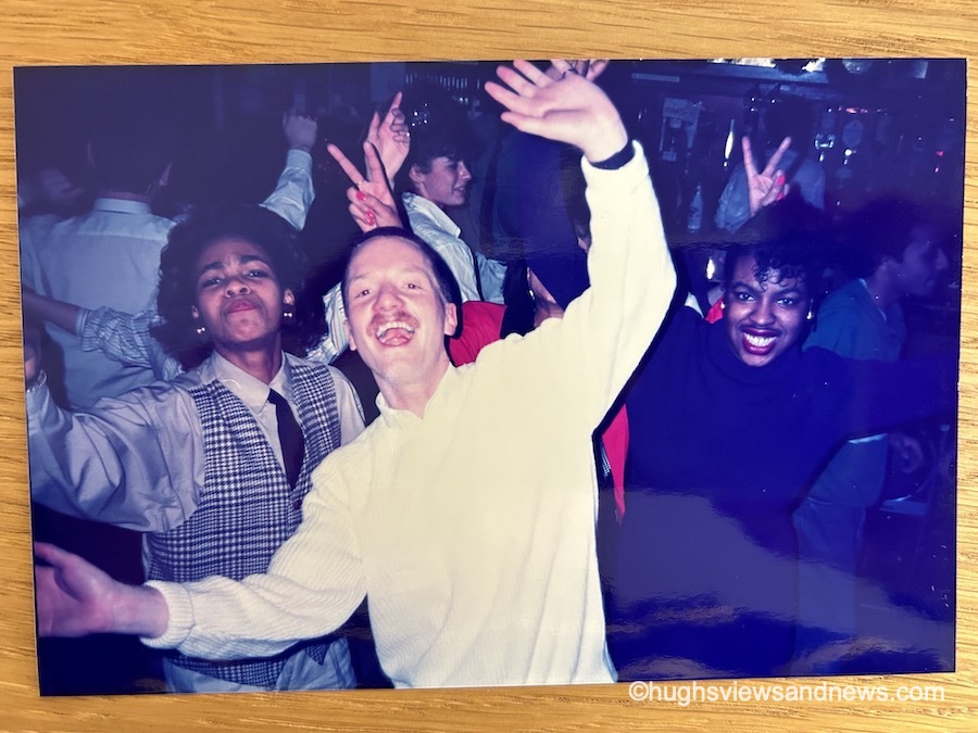 A photo of a young man and two young women either side of him, dancing with their hands in the air and having a great time on a crowded dance floor.