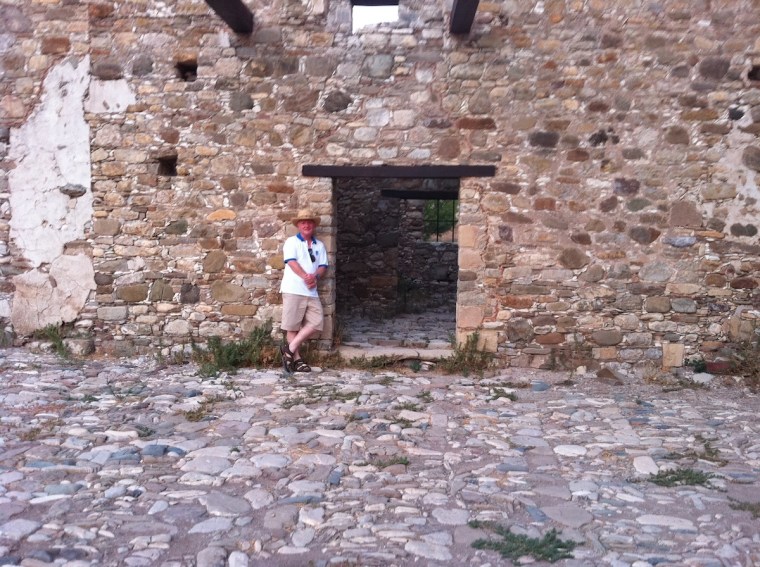 A photo of a man standing next to a gap in a wall that used to have a door. 